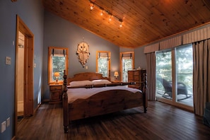 Ein Schlafzimmer mit einem hölzernen Bett, einem großen Fenster mit Vorhängen, einer Holzbalkendecke und einem Nachttisch mit Lampe.