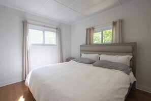 Une chambre à coucher avec un lit, deux fenêtres et une vue sur la verdure.
