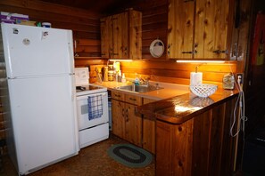 Eine Holzhütte mit einer Küche, inklusive Kühlschrank, Herd, Spüle und Holzschränken.