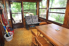 Ein Zimmer mit einem Holztisch, einem gepolsterten Stuhl, einem Fenster mit Blick auf Bäume und einer Tür, die nach draußen führt.