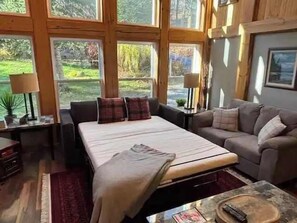 Ein Schlafzimmer mit einem Bett, zwei Sofas, einem kleinen Tisch und einem Fenster mit Blick auf Grünflächen.
