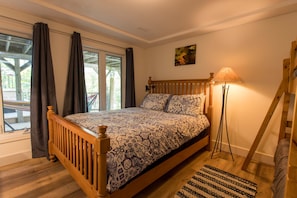 Ein Schlafzimmer mit einem hölzernen Bett, einer Stehlampe, Blick durch ein Fenster und einem Bild an der Wand.