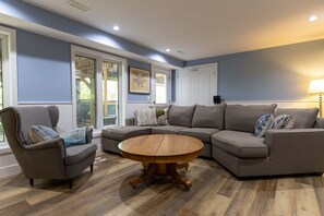 Ein Wohnzimmer mit einer Eckcouch, einem runden Holztisch und einem Couchtisch mit Glasplatte.