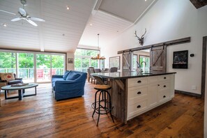 A spacious living area with a blue sofa, wooden flooring, a ceiling fan, and a large window overlooking greenery. - Penn Lake Sweet Grass Ontario (Huntsville)