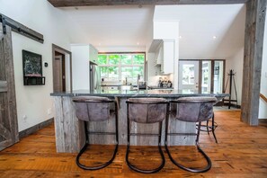 A kitchen with a bar area, wooden flooring, and a view of the outdoors. - Penn Lake Sweet Grass Ontario (Huntsville)