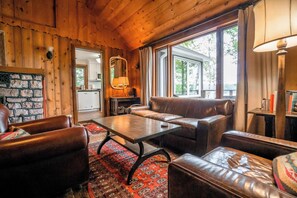 A cozy room with a stone fireplace, leather furniture, and large windows.