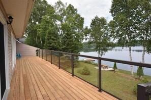 Eine Holzterrasse mit Glasgeländer, die auf einen See mit umliegenden Bäumen blickt.
