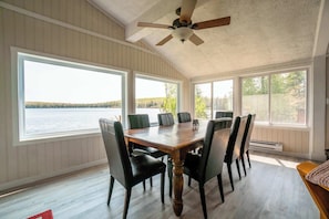 Ein Essbereich mit Holztisch und Stühlen, großen Fenstern mit Seeblick und einem Deckenventilator.