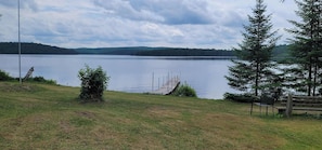 Blick auf einen See mit Steg, Rasenfläche und Bank.