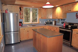 Eine Küche mit Holzausbau, einem Edelstahl-Kühlschrank, einer Mikrowelle, einem Backofen und einer Kochinsel mit Granitplatte.
