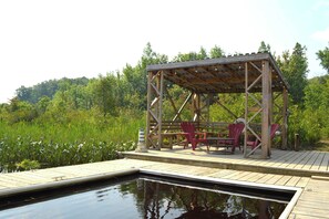 Eine Holzterrasse mit einem Pavillon, roten Stühlen und einem Pool.