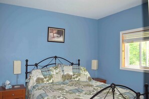 A bedroom with a bed, a nightstand, a bedside table, a window, and a picture on the wall. - Cecebe R and R Ontario (Burk's Falls)