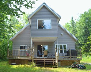 A two-story house with a front porch, a deck, and a large window. - Cecebe R and R Ontario (Burk's Falls)