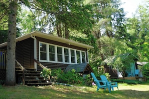 Eine Holzhütte mit großen Fenstern, einer Veranda mit blauen Stühlen und einer Treppe zum Eingang.