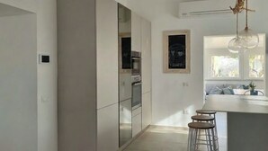 Une cuisine moderne avec des meubles blancs, un luminaire suspendu et un coin bar avec des tabourets.