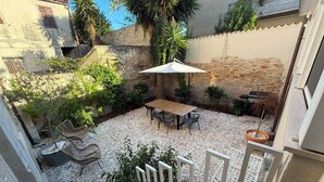 Une cour avec une table et des chaises, entourée de plantes et agrémentée d’un barbecue.