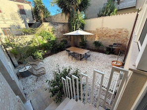 Un cortile con tavolo e sedie, circondato da piante e un barbecue.