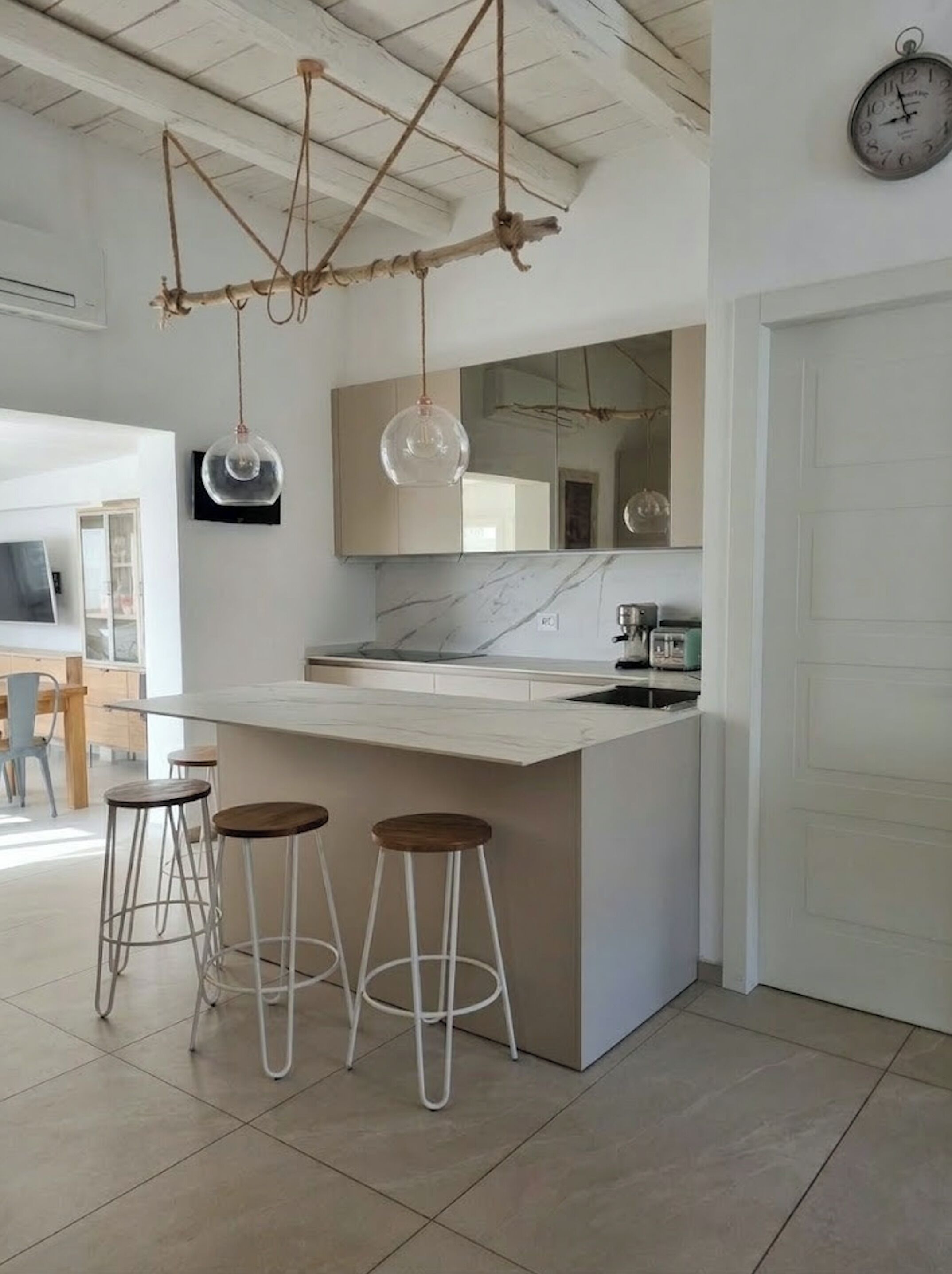 Une cuisine moderne avec un plan de travail en marbre, des luminaires suspendus et un grand miroir au-dessus de l’îlot central.