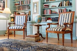 A room with two wooden chairs with striped upholstery, a globe on a small table, and bookshelves filled with books. - The Rourk House | Historic 1927 Southern Home (Shallotte)