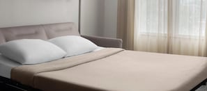 Una cama con cabecera, una manta y una ventana con cortinas traslúcidas.