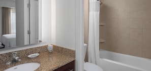 A bathroom with a granite countertop, two sinks, a mirror, a shower curtain, and a bathtub.