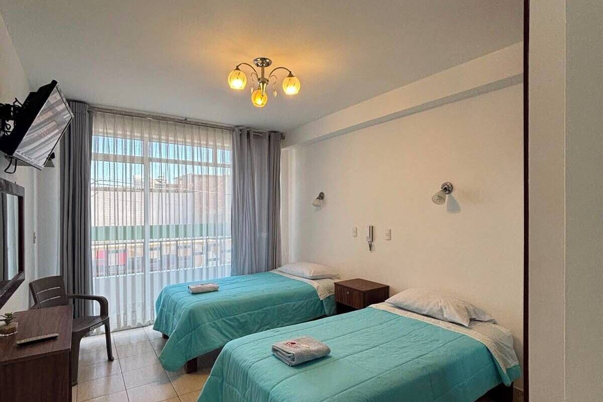 A hotel room with two beds, a desk, a chair, a lamp, and a window with curtains.