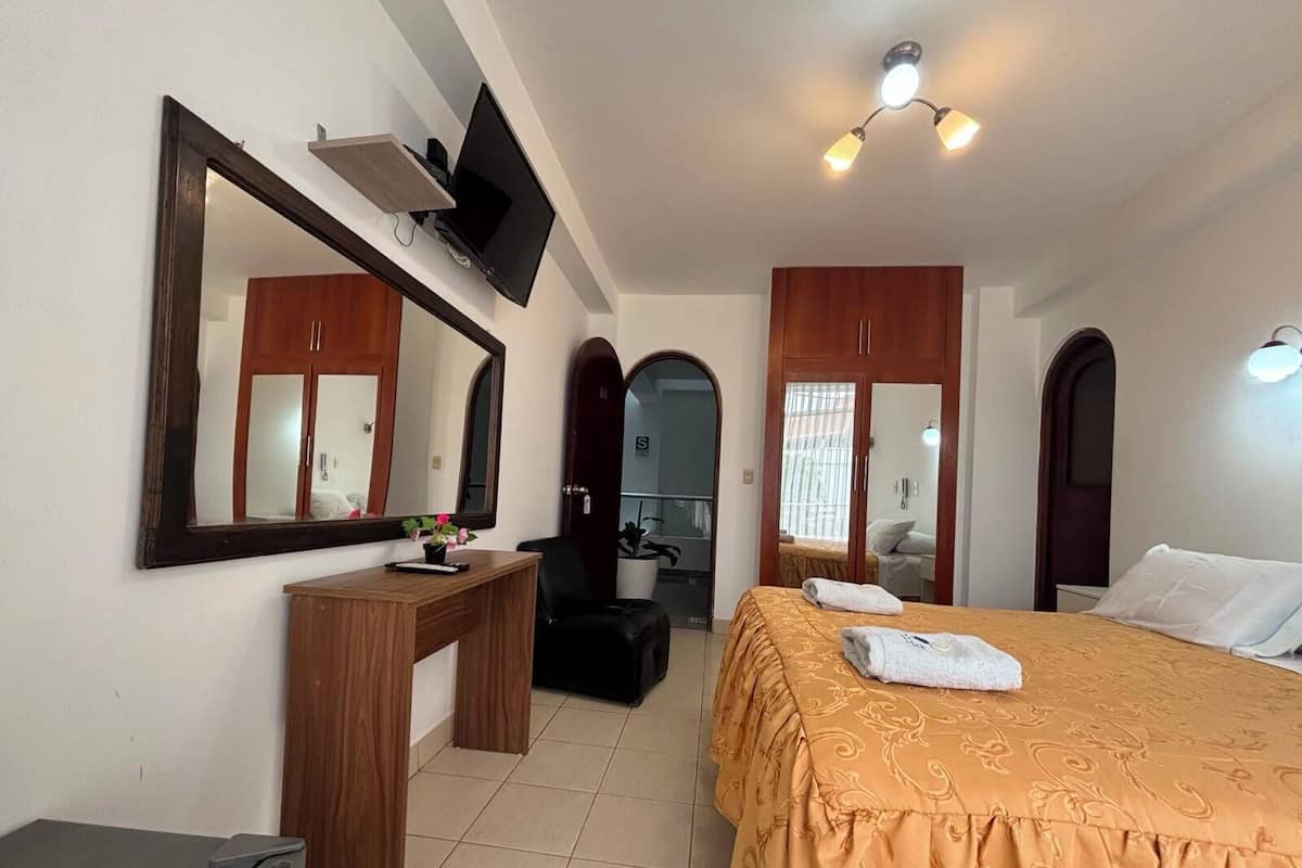 Ein Hotelzimmer mit Bett, Schreibtisch, Stuhl, Fernseher und Spiegel.