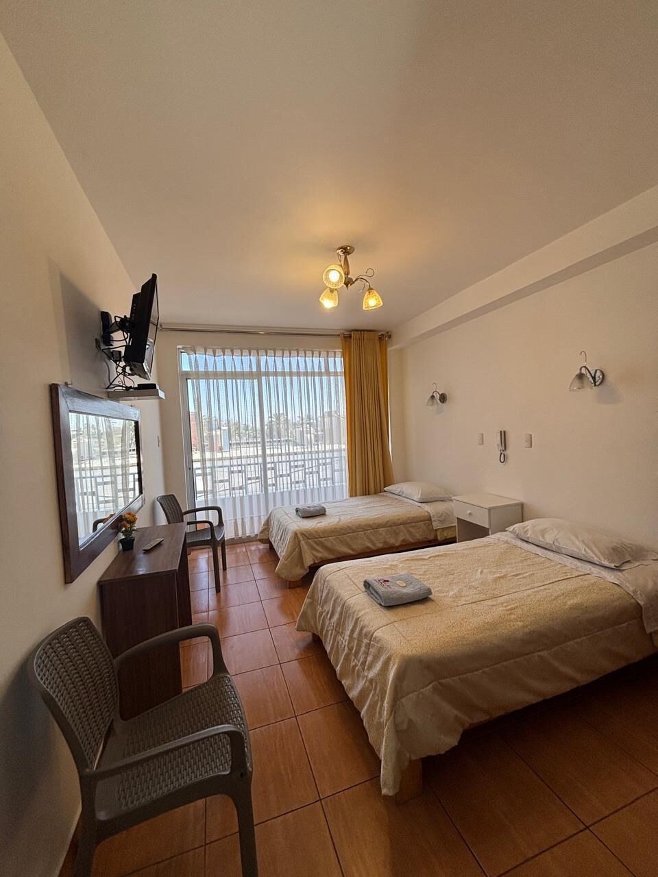 A hotel room with two beds, a desk with a chair, a TV, and a window with curtains.