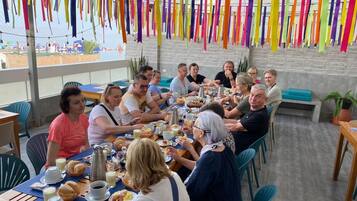 Un grupo de personas cenando en una mesa con vistas a la playa, rodeado de decoraciones colgantes de colores.