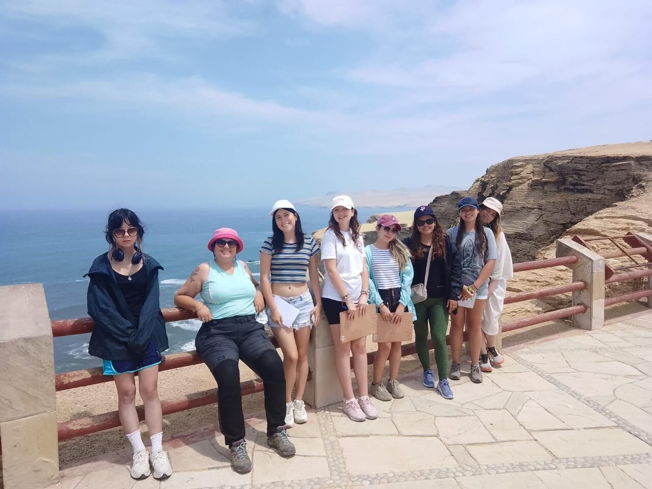 A group of people standing on a stone pathway by a coastal area with a rocky cliff and ocean view.