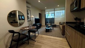 Uma sala de estar moderna com uma mesa redonda, duas cadeiras, um sofá, uma televisão e uma área de cozinha com micro-ondas.