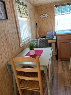 A wooden interior with a dining table, chairs, a potted plant, and a kitchen area with a window.