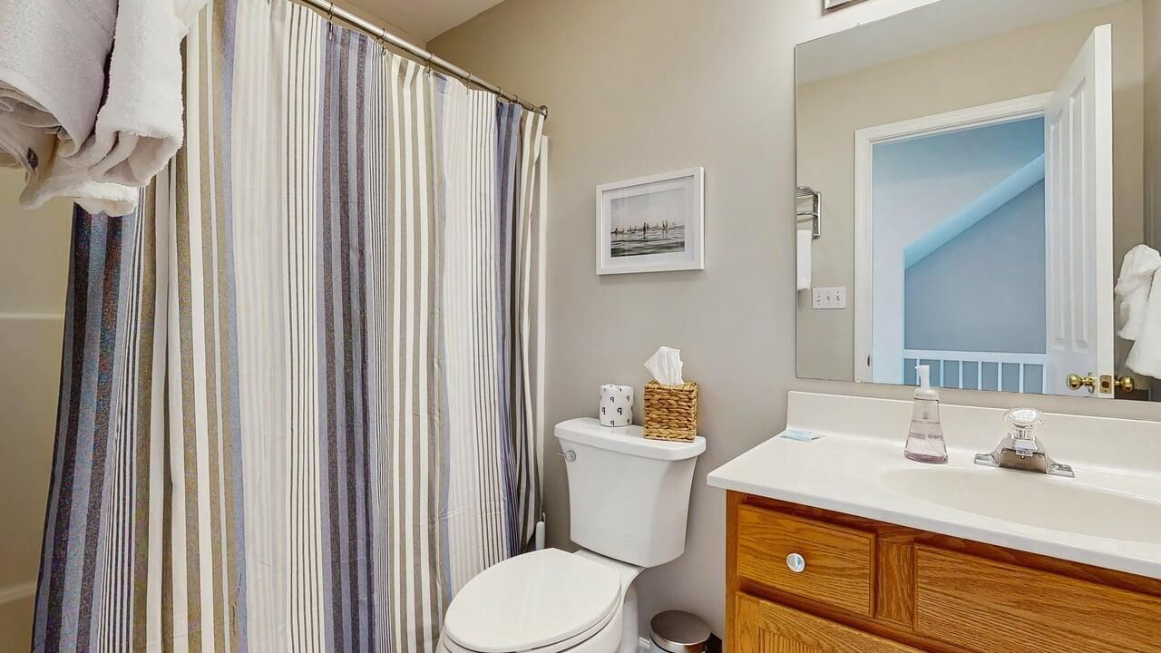 A bathroom with a striped shower curtain, a toilet, a sink with a mirror, and a framed picture on the wall.