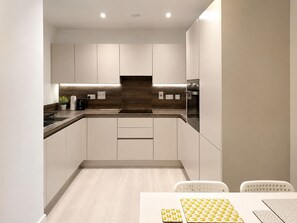 A modern kitchen with white cabinets, a wooden backsplash, and a built-in oven. - 1BR City Escape | Free Gym | Wembley & Kings Cross (London)