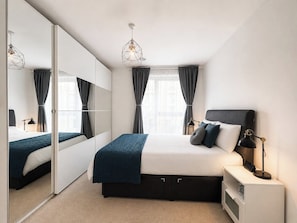 Ein modernes Schlafzimmer mit einem großen Bett, Nachttischen, einem Spiegel und einer Pendelleuchte.
