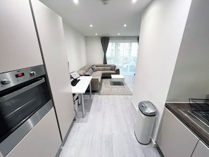 Eine moderne Küche mit Einbauofen, ein Essbereich mit Tisch und Stühlen, eine Sitzecke und Blick durch ein großes Fenster.