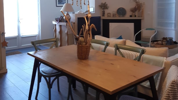 A dining area with a wooden table, chairs, hanging light fixtures, and a fireplace. - B&B with breakfast (Lège-Cap-Ferret)