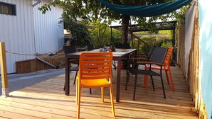 A wooden deck with a table and chairs, surrounded by greenery and a white building. - B&B with breakfast (Lège-Cap-Ferret)