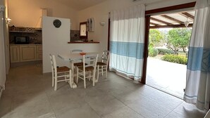 A kitchen with a microwave, a sink, and a window. There is a dining area with a table and chairs. - Costa Serena Village (Porto Rafael, Palau)