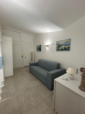 A room with a grey sofa, a white desk with a lamp, and two paintings on the wall.