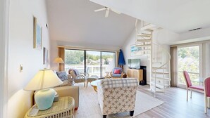 Un vaste salon doté d’un escalier, de grandes fenêtres et offrant une vue sur l’extérieur.