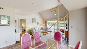Un vaste salon agrémenté d’un escalier en colimaçon, un coin repas avec des chaises roses et une vue sur l’extérieur.
