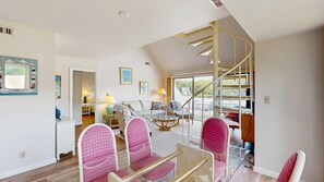 Ein geräumiges Wohnzimmer mit einer Wendeltreppe, einem Essbereich mit rosafarbenen Stühlen und Blick ins Freie.