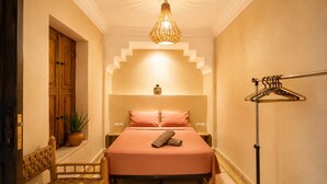 A bedroom with a bed, a hanging light fixture, a wooden wardrobe, a potted plant, and a wooden chair. - 2-bedroom riad in enchanting Marrakech with cool AC breeze (Marrakech)