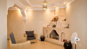 A living room with a fireplace, wicker furniture, a yellow rug, and a ceiling light fixture. - 2-bedroom riad in enchanting Marrakech with cool AC breeze (Marrakech)
