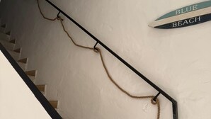 A staircase with a rope hanging from the handrail, a sign reading 'BLUE BEACH' on the wall, and a plant on the right.