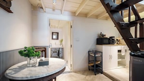 Una cocina con una mesa redonda de mármol, una silla de madera, un armario negro y una escalera.