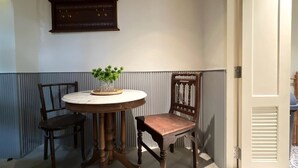 Habitación de esquina con una mesa redonda, dos sillas, una planta en maceta y una placa en la pared.