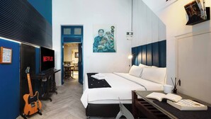 Una habitación de hotel moderna con cama, escritorio, guitarra, televisor y un cuadro en la pared.