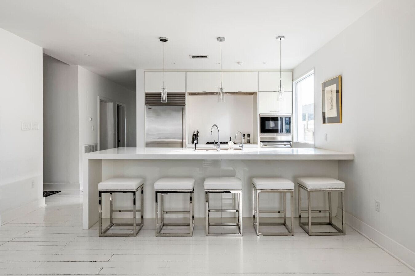 A modern kitchen with a large island, bar stools, pendant lights, and a microwave.